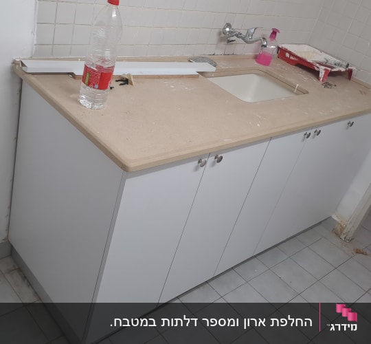 ארון מטבח לבן מותקן עם משטח עבודה, כיור וצוקל בתחתית